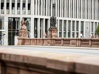 a man walks across the street in front of a stone lion statue and some building