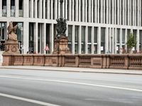 a man walks across the street in front of a stone lion statue and some building