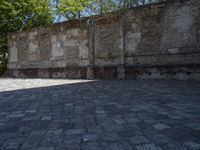 a man walking on the ground past an old wall in a city park setting with a stone floor and a stone bench