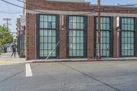 a man with a skateboard walks down the street by a store and a brick building