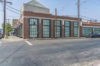 a man with a skateboard walks down the street by a store and a brick building