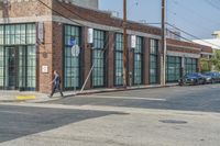 a man with a skateboard walks down the street by a store and a brick building