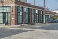 a man with a skateboard walks down the street by a store and a brick building