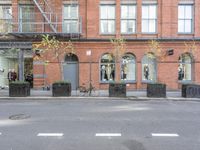 an empty street and bicycle parked outside of a store front window and behind planters