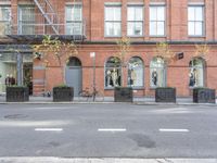 an empty street and bicycle parked outside of a store front window and behind planters