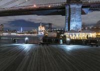 a pier by the brooklyn bridge at night with some people on it and a bus that's driving down the street