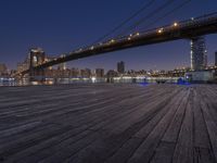 a photo of the brooklyn bridge taken from the docks at night, with lights on the bridge