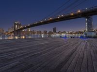 a photo of the brooklyn bridge taken from the docks at night, with lights on the bridge