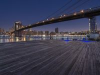 a photo of the brooklyn bridge taken from the docks at night, with lights on the bridge