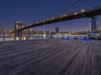 a photo of the brooklyn bridge taken from the docks at night, with lights on the bridge