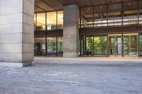an empty brick parking lot in front of a tall building with lots of glass doors