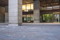 an empty brick parking lot in front of a tall building with lots of glass doors