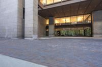 an empty brick parking lot in front of a tall building with lots of glass doors