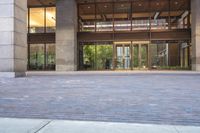 an empty brick parking lot in front of a tall building with lots of glass doors
