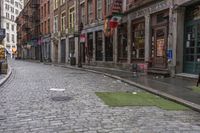 the cobblestone street in front of stores along a city side walk with people walking by