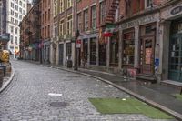 the cobblestone street in front of stores along a city side walk with people walking by