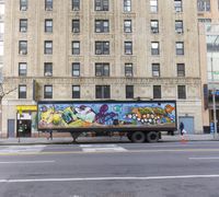 a truck painted with different kinds of graffiti parked in front of a large building on the corner