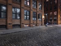 a row of old brick buildings at night on a cobble stone street with street lamps