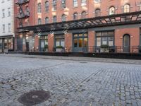 a red fire hydrant sitting in the middle of a brick street and next to tall buildings