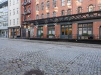 a red fire hydrant sitting in the middle of a brick street and next to tall buildings