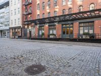 a red fire hydrant sitting in the middle of a brick street and next to tall buildings