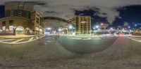 a street is dimly lit up at night time, with the buildings behind the circle of empty cars