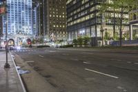 an empty street in the city surrounded by tall buildings at night with people waiting to cross