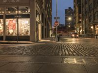 the stop sign stands at a corner on the sidewalk of this city block at dusk
