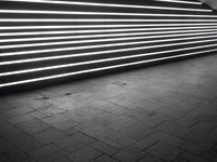 lights shine brightly inside the tunnel that has dark brick flooring and walls and is surrounded by black tiles