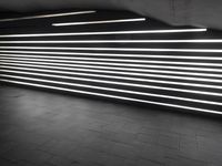 lights shine brightly inside the tunnel that has dark brick flooring and walls and is surrounded by black tiles