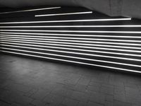 lights shine brightly inside the tunnel that has dark brick flooring and walls and is surrounded by black tiles