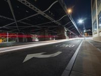 a car passes under the highway under an overpass at night, with light trails coming from underneath