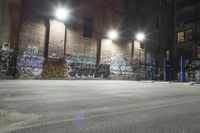 an empty parking lot covered with graffiti and lights at night in a factory district area