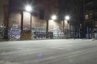 an empty parking lot covered with graffiti and lights at night in a factory district area