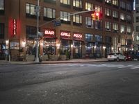 cars are waiting at a red light outside of a bar grill pizza restaurant in the city