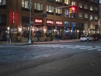 cars are waiting at a red light outside of a bar grill pizza restaurant in the city