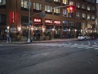 cars are waiting at a red light outside of a bar grill pizza restaurant in the city