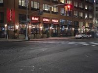 cars are waiting at a red light outside of a bar grill pizza restaurant in the city