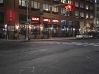 cars are waiting at a red light outside of a bar grill pizza restaurant in the city