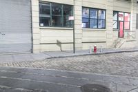 a fire hydrant on the sidewalk of a small street, in front of a building with a roller gate