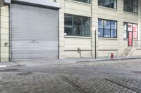 a fire hydrant on the sidewalk of a small street, in front of a building with a roller gate