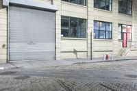 a fire hydrant on the sidewalk of a small street, in front of a building with a roller gate