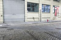a fire hydrant on the sidewalk of a small street, in front of a building with a roller gate
