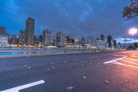 an empty road on a city street near the water at night, with streetlights glowing down