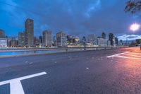 an empty road on a city street near the water at night, with streetlights glowing down