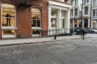 two people walk through an alley near brick buildings on a city street with car parking spaces