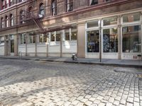 a fire hydrant stands outside a storefront in the city on an empty brick street