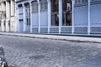 a person is sitting on an empty bench in a narrow alley with blue buildings on either side