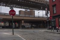 a stop sign with the brooklyn bridge above it in the background at an intersection under a bridge