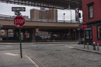 a stop sign with the brooklyn bridge above it in the background at an intersection under a bridge